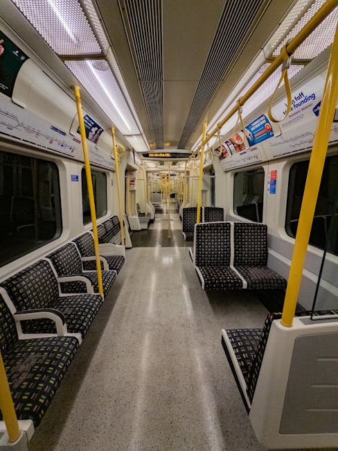 Interior view of an empty train carriage at night, featuring a clean, well-maintained floor made of speckled grey vinyl material. The carriage has rows of black fabric-covered seats with colorful geom